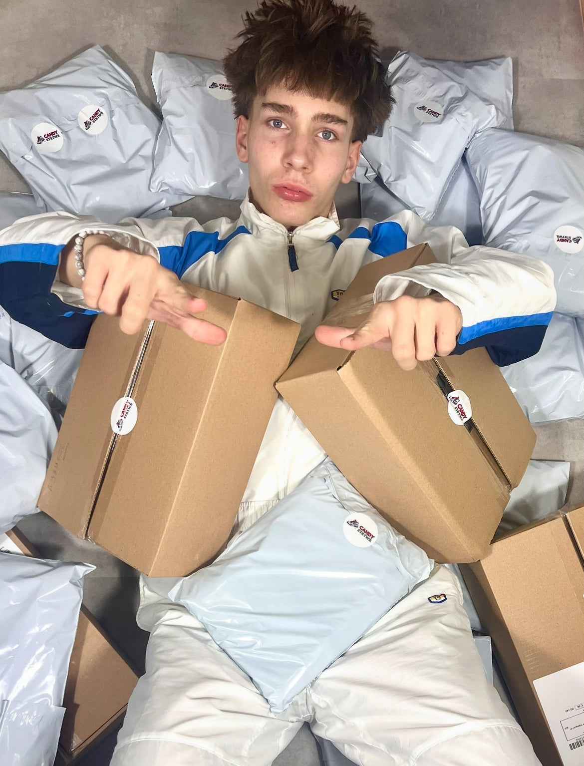 Fiatal férfi fehér streetwear melegítőben csomagokkal vintage designer ruhák körében